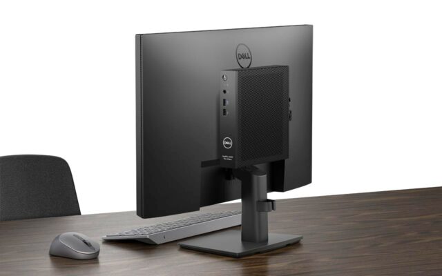 Dell Optiplex 3000 thin client positioned on back of a Dell 24" monitor on a walnut colored desk.