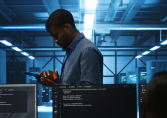 Technician doing system analysis using tablet, doing needed adjustments in supercomputers server farm. Engineer overseeing data center housing storage infrastructure supporting critical IT workloads